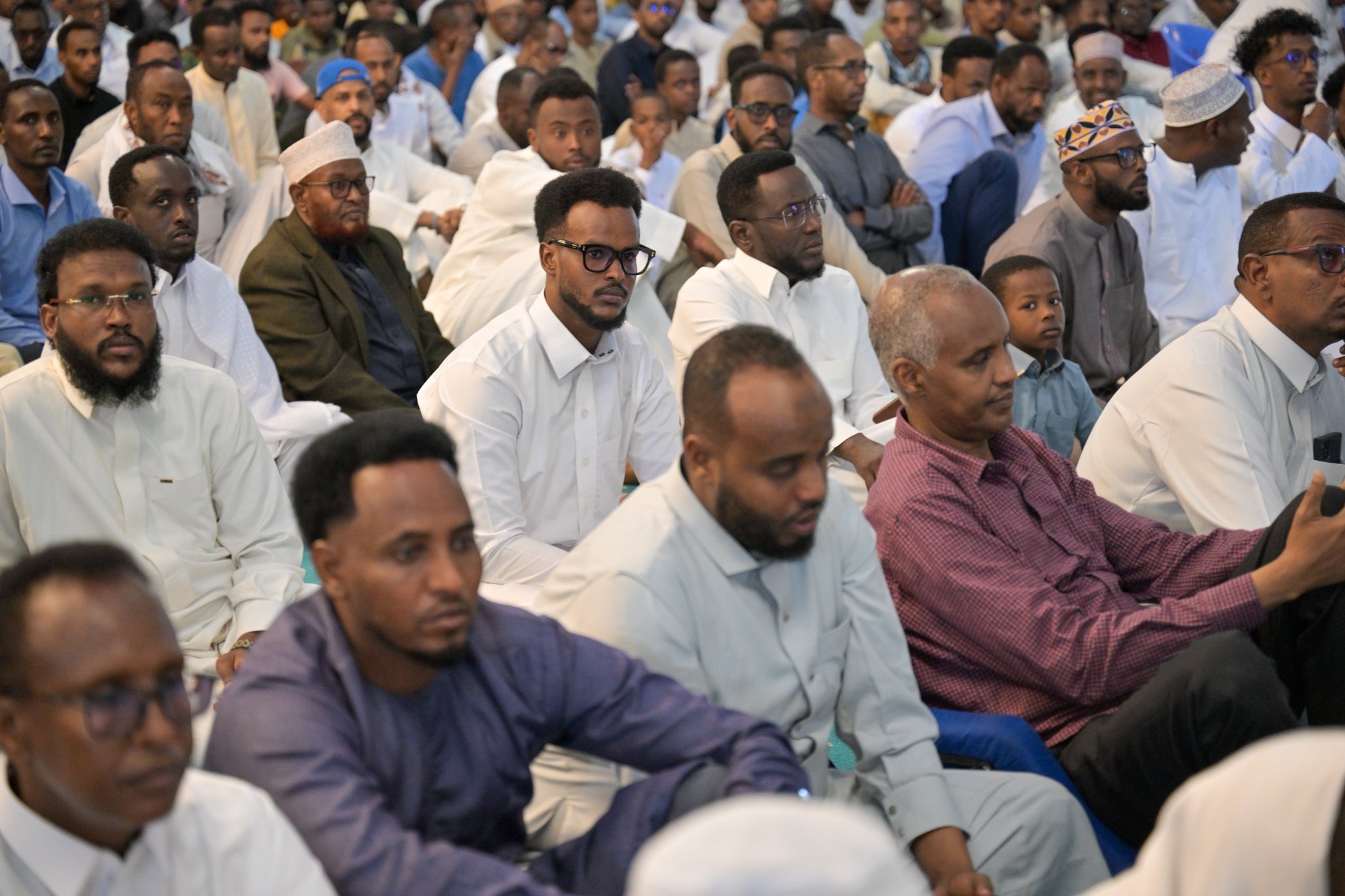 A large crowd of East African men sitting close together and listening Friday sermon from the pulpit of the Grand Mosque in the Somali capital, delivers by Secretary-General of the MWL